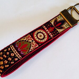 May include: A red, black, and gold patterned key chain with a brass key ring.