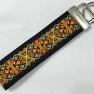 May include: A black key chain with a silver key ring. The key chain is decorated with a colorful pattern of orange, yellow, and green.