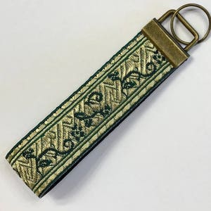 May include: A green and gold key chain with a floral design. The key chain has a brass key ring.