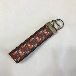 May include: A brown key chain with a fox print and a gold metal key ring.