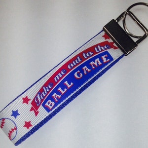 May include: White and blue key chain with a red, white, and blue ribbon that says "Take me out to the ball game". The ribbon has a baseball graphic and stars.