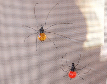 May include: Three wire spiders with different colored glass beads for their bodies. The spiders are orange, red, and green.