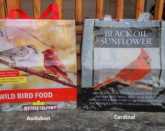May include: Two reusable shopping bags with bird seed. The bag on the left has a red, white, and blue design with the text "WILD BIRD FOOD" and "Audubon". The bag on the right has a blue and gray design with the text "BLACK OIL SUNFLOWER" and "Cardinal".