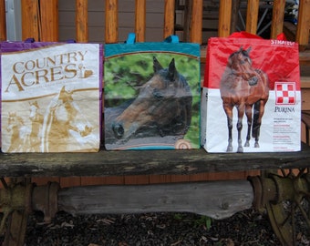 May include: Three reusable shopping bags with horse images. The bag on the left is purple and says "Country Acres". The middle bag is blue and has a brown horse head. The bag on the right is red and says "Purina" with a white checkerboard logo.
