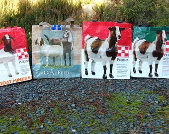 May include: Four reusable shopping bags with a goat theme. Each bag features a different goat breed and the Purina brand logo. The bags are white with red, green, and blue accents. The text on the bags reads "Purina Goat Feed", "Purina Goat Mineral", and "Purina".