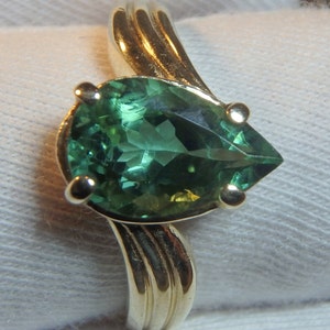 May include: A gold ring with a pear-shaped green gemstone. The ring has a simple, elegant design.