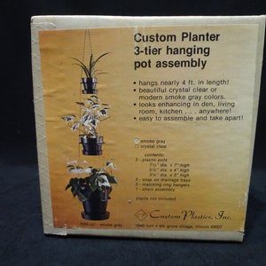 May include: A three-tier hanging planter assembly made of smoke gray plastic. The planter hangs nearly 4 feet long and includes three pots, three drainage trays, three ring hangers, a chain assembly, and instructions. Plants are not included. Custom Plastics, Inc. 1940 Lunt Elk Grove Village, Illinois 60007