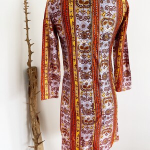 May include: A vintage 1960s dress with a colorful floral and geometric pattern. The dress has a long sleeve and a fitted silhouette. The fabric is a blend of polyester and cotton.