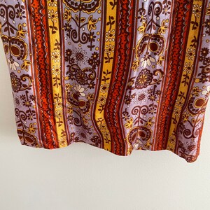 May include: A close-up of a fabric with a striped pattern. The stripes are in shades of orange, brown, yellow, and purple. The fabric is covered in a floral pattern.