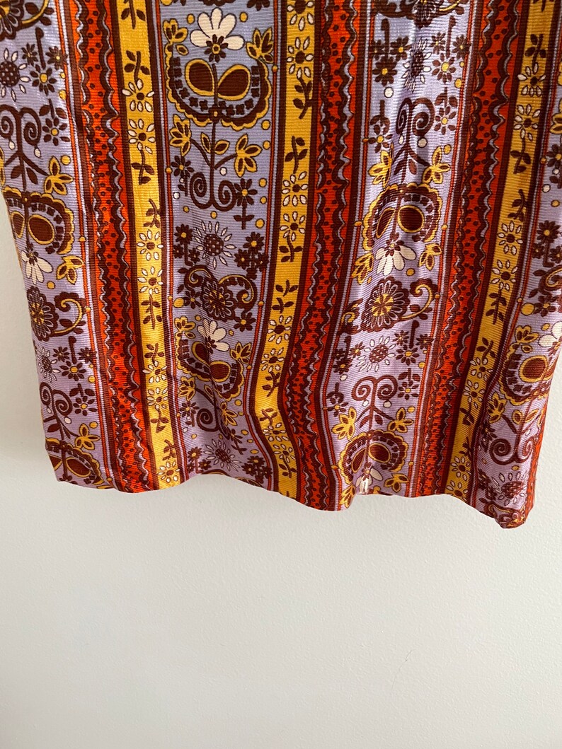 May include: A close-up of a fabric with a striped pattern. The stripes are in shades of orange, brown, yellow, and purple. The fabric is covered in a floral pattern.