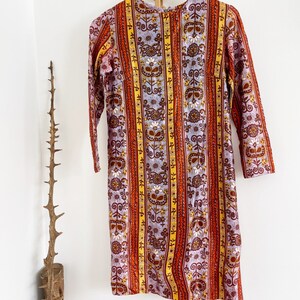 May include: A vintage dress with a colorful striped pattern featuring floral and geometric designs in shades of orange, yellow, brown, and purple.