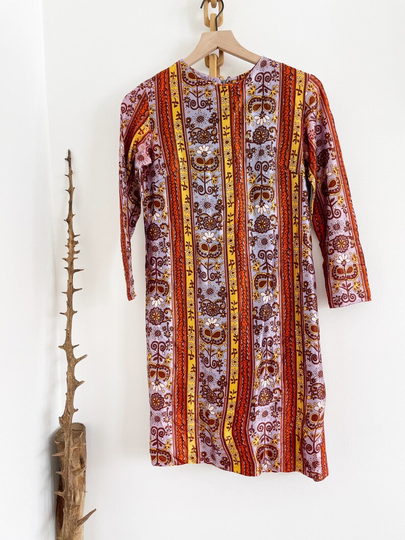 May include: A vintage dress with a colorful striped pattern featuring floral and geometric designs in shades of orange, yellow, brown, and purple.