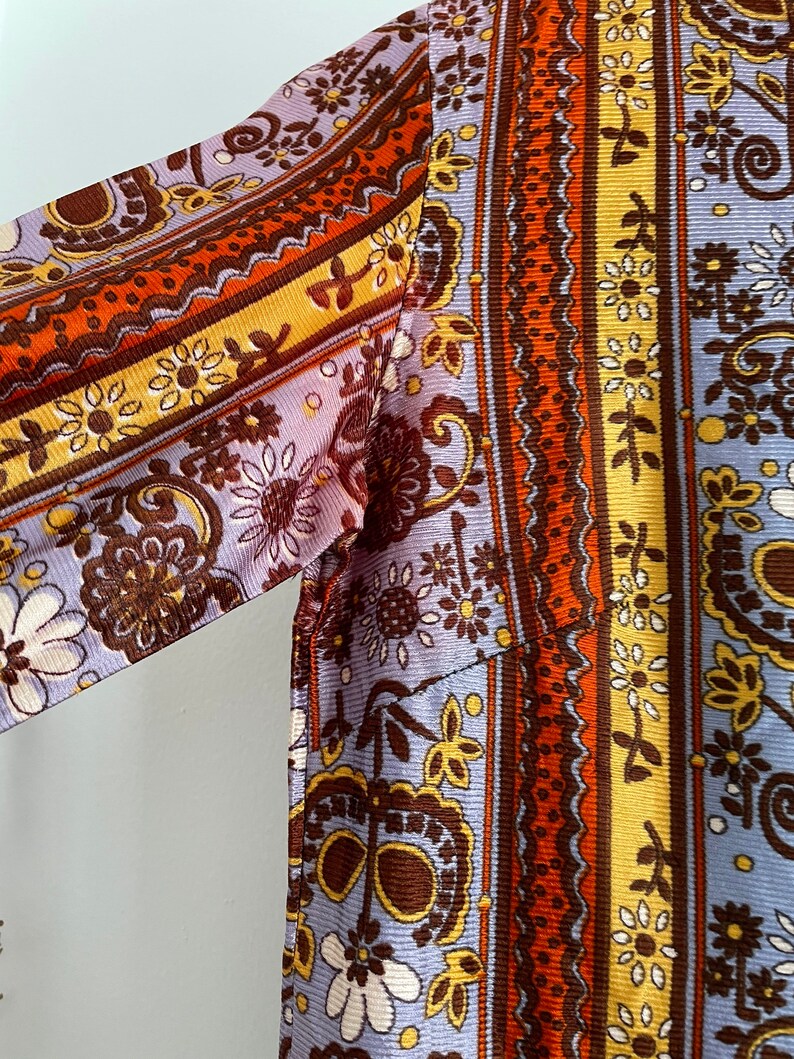 May include: A long-sleeved shirt with a paisley pattern in shades of brown, orange, yellow, and white on a light purple background.