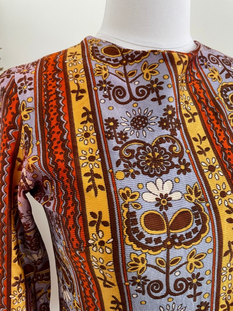 May include: A long-sleeved shirt with a vintage floral pattern in shades of brown, orange, yellow, and blue. The pattern features flowers, leaves, and swirls.