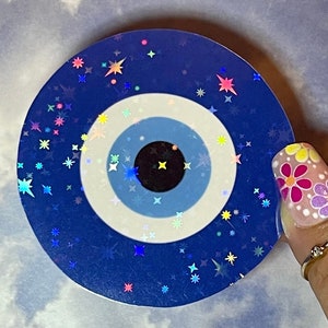 May include: A blue and white evil eye sticker with a holographic finish and a scattering of rainbow stars.