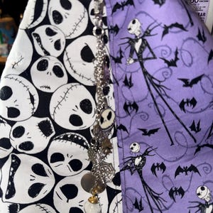 May include: A split fabric item featuring a black and white Jack Skellington pattern on one side and a purple fabric with Jack Skellington and bat silhouettes on the other. A decorative charm hangs in front.