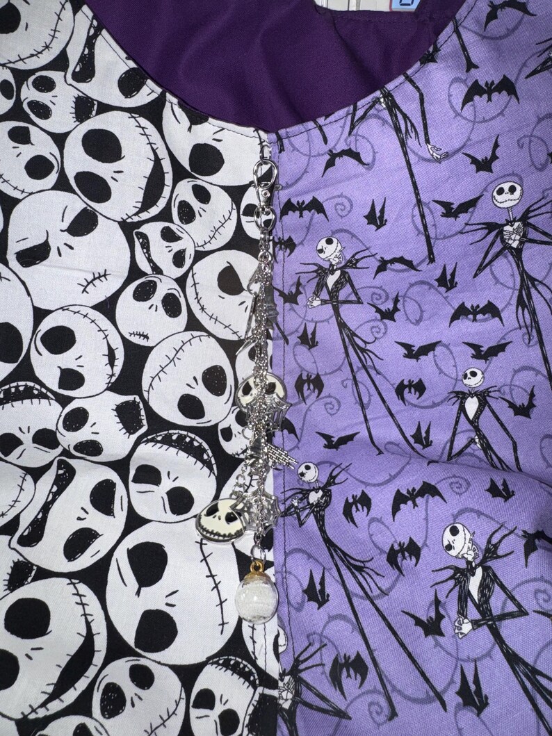 May include: A split-design fabric featuring a black and white skull pattern on one side and a purple pattern with Jack Skellington and bats on the other. A decorative chain with skull charms and a clear orb hangs from the center.