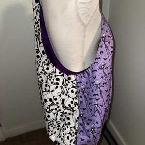 May include: A large tote bag with a purple interior and a split design. One side features a pattern of white skulls on a black background, while the other side has a purple background with Jack Skellington and bat silhouettes.