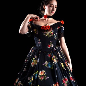 May include: A black floral print dress with a fitted bodice and a full skirt. The dress features off-the-shoulder sleeves with fringe and is adorned with red flower accents. A black choker with a red flower is also visible.