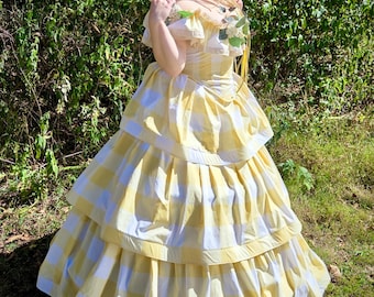 May include: A yellow and white checkered dress with a tiered skirt and off-the-shoulder sleeves. The dress is adorned with floral accents and a matching flower crown. The dress is a vintage style, perfect for a costume or special event.