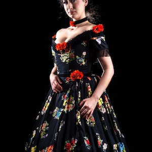 May include: A black floral print dress with a sweetheart neckline and off-the-shoulder sleeves. The dress features red flower accents and fringe detailing. The full skirt is adorned with colorful floral patterns, creating a romantic and elegant look.