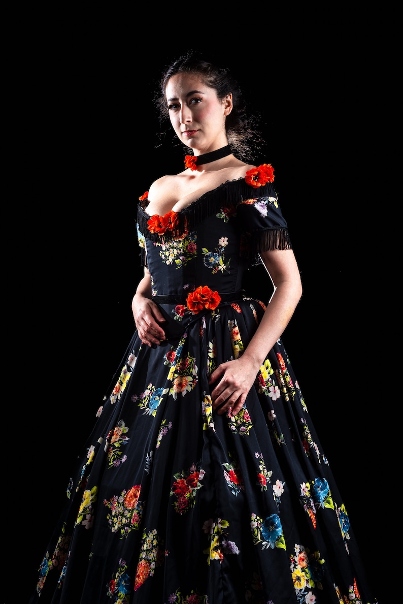 May include: A black floral print dress with a sweetheart neckline and off-the-shoulder sleeves. The dress features red flower accents and fringe detailing. The full skirt is adorned with colorful floral patterns, creating a romantic and elegant look.