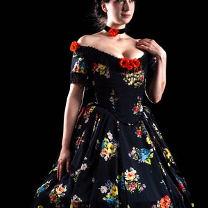 May include: A black off-the-shoulder gown with a floral pattern in red, yellow, blue, and white. The dress features a fitted bodice, a full skirt, and is adorned with red flower accents. A black choker with a red flower is also visible.