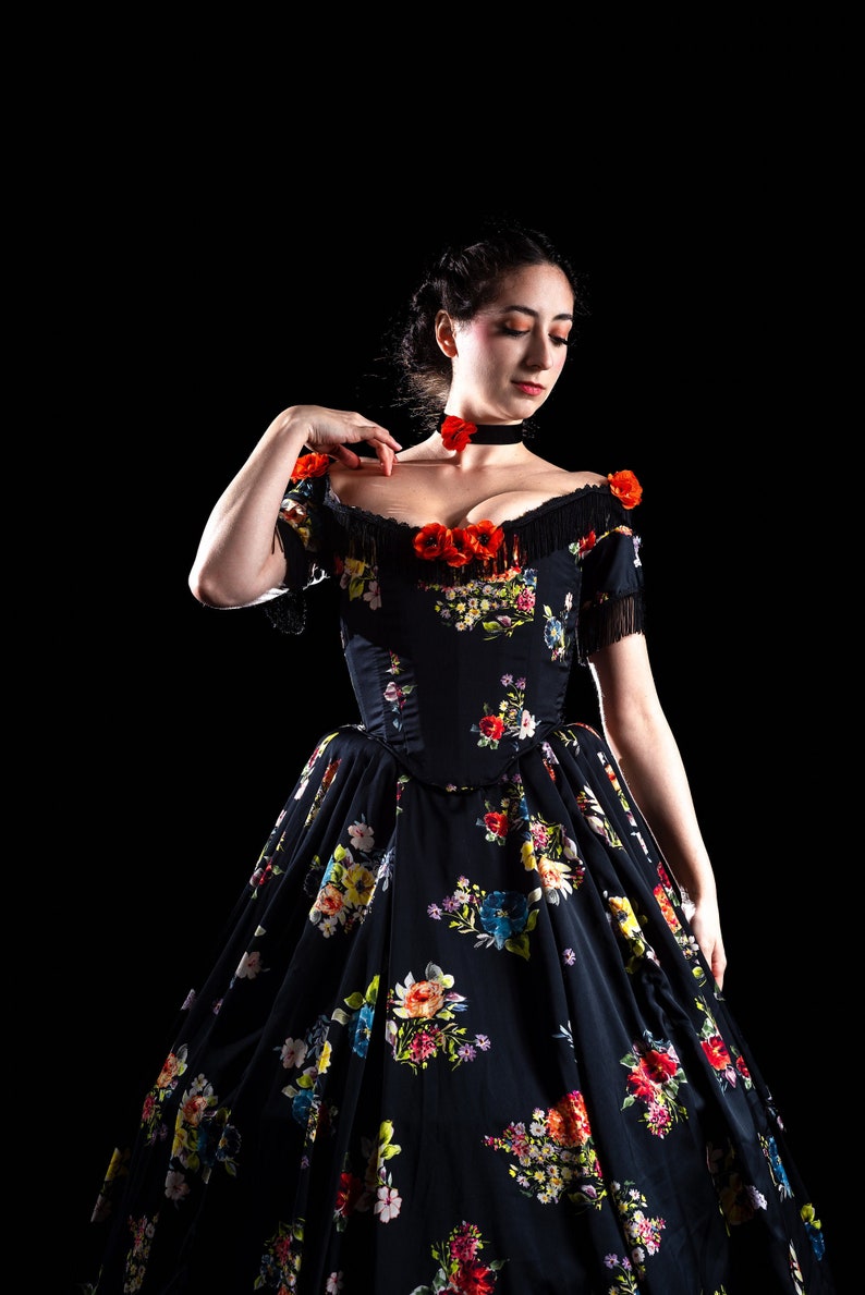 May include: A black floral print dress with a fitted bodice and a full skirt. The dress features off-the-shoulder sleeves with fringe and is adorned with red flower accents. A black choker with a red flower is also visible.