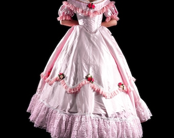 May include: A light pink ball gown with a fitted bodice and a full skirt. The dress features ruffled sleeves, lace trim, and floral accents. The skirt has a lace hemline and is made of a shiny fabric. The dress is designed for a formal event.