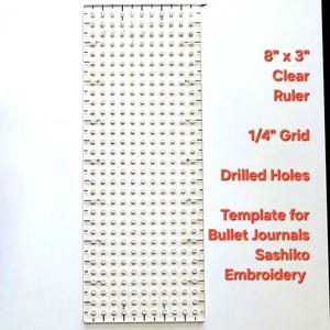 May include: A clear plastic ruler, 8 inches by 3 inches, with a 1/4 inch grid and drilled holes. The ruler is designed as a template for bullet journals and Sashiko embroidery.