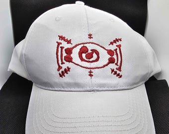 May include: White baseball cap with a red embroidered design on the front. The cap has a curved brim and a structured crown. The embroidered design appears to be a stylized eye or symbol.