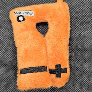 May include: Orange plush toy with a heart-shaped cutout and a black cross design. The toy has the words "Add Water" printed on it. The toy has a small orange tab at the top.