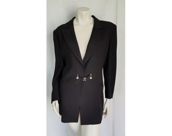May include: A solid black blazer featuring long sleeves, a notched lapel collar, and a single metallic clasp closure at the waist. The garment has a structured shoulder design and a straight hemline, presented on a neutral-toned mannequin form.