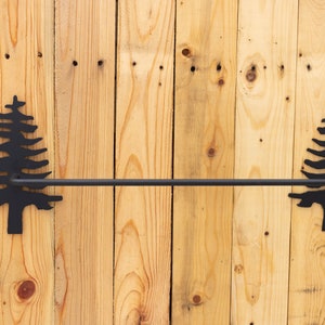 May include: Black metal towel bar with pine tree silhouettes on each end, mounted on a wood wall.