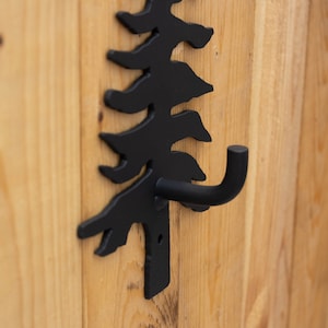 May include: Black metal hook shaped like a pine tree, mounted on a wooden surface.