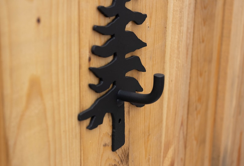 May include: Black metal hook shaped like a pine tree, mounted on a wooden surface.