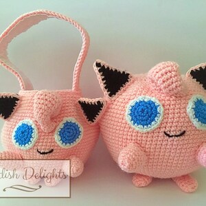 May include: A pink crocheted  Jigglypuff plushie with black ears and blue eyes.  There is a smaller pink crocheted Jigglypuff basket with a handle.