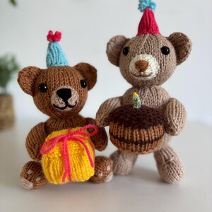 May include: Two knitted teddy bears wearing small party hats. The bear on the left is dark brown and holds a yellow gift box with pink yarn ribbon. The bear on the right is light brown and holds a brown cake with a single yellow candle on top.