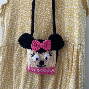 Pu&ograve; includere: Una piccola borsa a mano in maglia con un design Minnie Mouse nero e rosa. La borsa ha una tracolla nera ed &egrave; realizzata in filato.