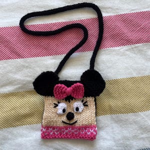 Pu&ograve; includere: Una piccola borsa di maglia con una tracolla nera, a forma di topo dei cartoni animati con orecchie nere, un fiocco rosa e un fondo a righe bianco e rosa.