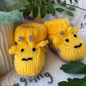 Könnte beinhalten: Ein Paar gelbe gestrickte Babyschuhe in Giraffenform mit braunen Flecken und schwarzen Augen.