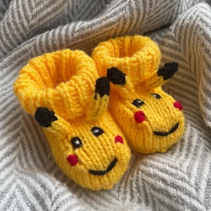 May include: A pair of yellow knitted baby booties with black and red details, shaped like Pikachu, a popular cartoon character.