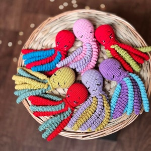 Könnte beinhalten: Eine Gruppe von acht gehäkelten Octopus-Plüschtieren in einem Weidenkorb. Die Octopus-Plüschtiere sind in verschiedenen Farben, darunter Rot, Rosa, Lila, Blau, Grün und Gelb.