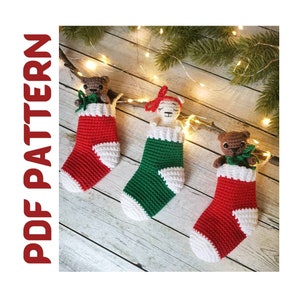 Può includere: Tre calze di Natale all'uncinetto con diversi personaggi di animali al loro interno. Le calze sono rosse, verdi e bianche. Gli animali sono un orso marrone, un lama bianco e un orso marrone.