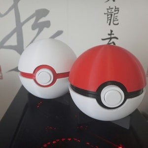 Op de afbeelding: Twee Poké Balls, één rood en één wit, met een zwarte ring rond het midden en een witte knop in het midden.