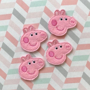 May include: Four pink felt embroidered patches shaped like the head of a cartoon pig. Each patch features two ears, two eyes, a snout with two nostrils, and a circular cheek detail. The embroidery is done in pink thread on a light pink felt base.