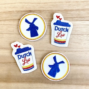 May include: Four embroidered patches with a Dutch theme. Two patches are circular with a blue windmill design inside a white circle, outlined in yellow and red. The other two patches are coffee cup shaped with the text "Dutch Luv" and red hearts.
