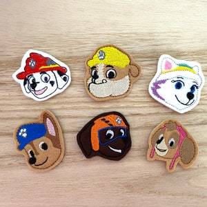 May include: Set of six embroidered patches featuring characters from a popular animated series. Each patch depicts a different dog character with distinct features, including hats and uniforms. The patches are in various colors, including red, blue, and brown.