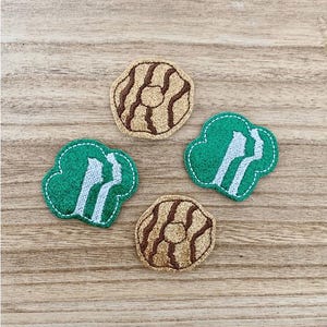 May include: Four embroidered patches consisting of two circular tan patches with brown stitched swirl patterns and two green clover-shaped patches featuring white stitched silhouettes of two figures facing each other with a white stitched border.