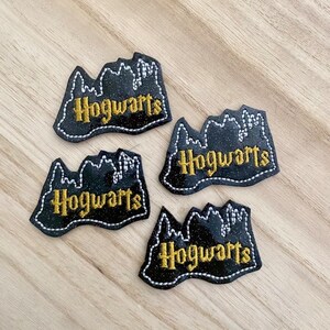 May include: Four black Hogwarts patches with gold lettering and a white stitched border. The patches feature a castle design. The patches are arranged on a light wood surface.